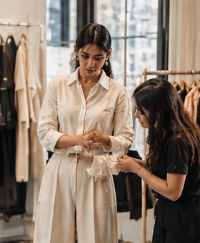 Two women look closely at the cuff of an ivory shirt in a bright boutique